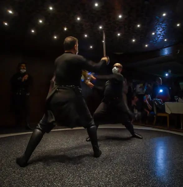 Two performers in black costume dancing with swords under low lighting