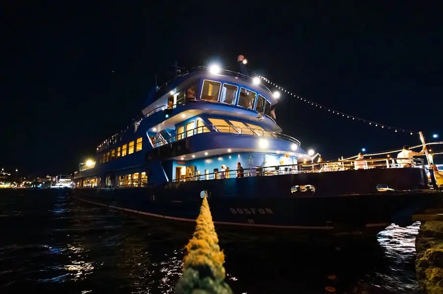 Guests on the BOSFOR's aft deck at night, string lights strung along the mast