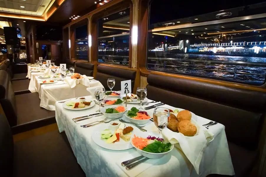 Starter plates and a bread basket on a table aboard the BOSFOR, city lights through the window