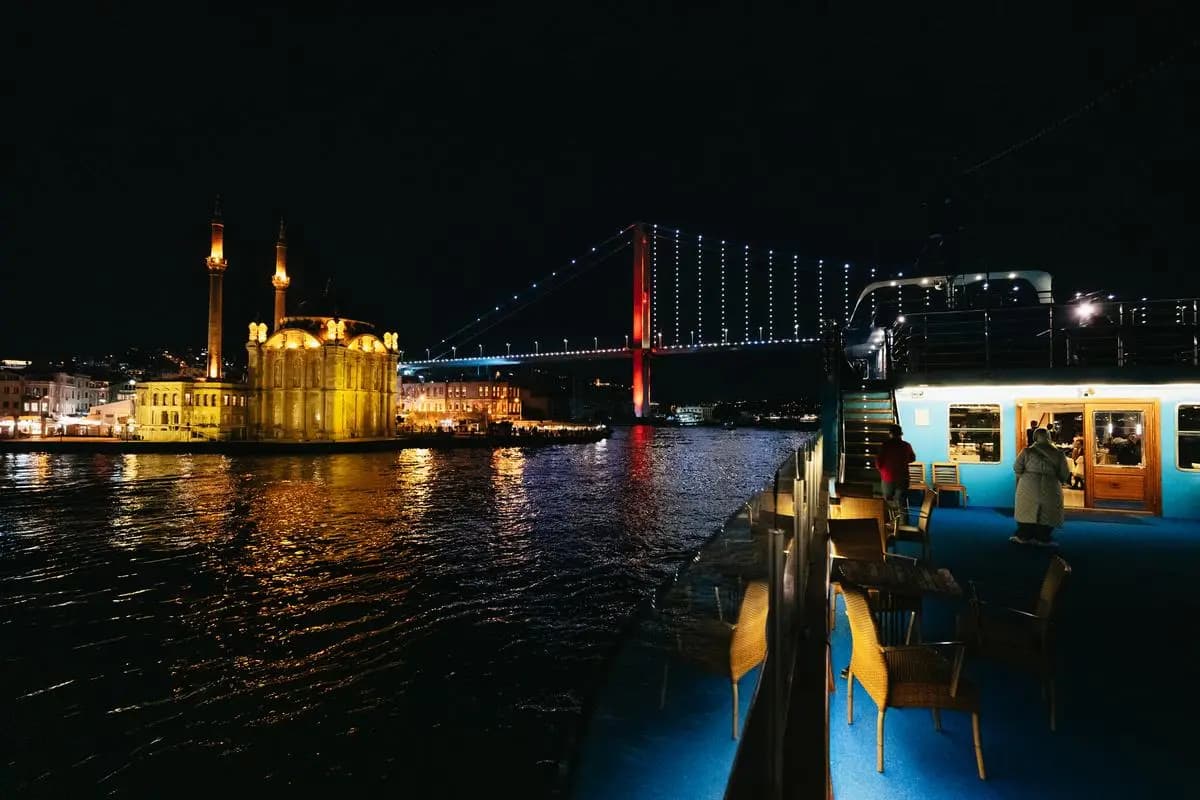 Guests at the rail of the BOSFOR at night, the lit shoreline across the water