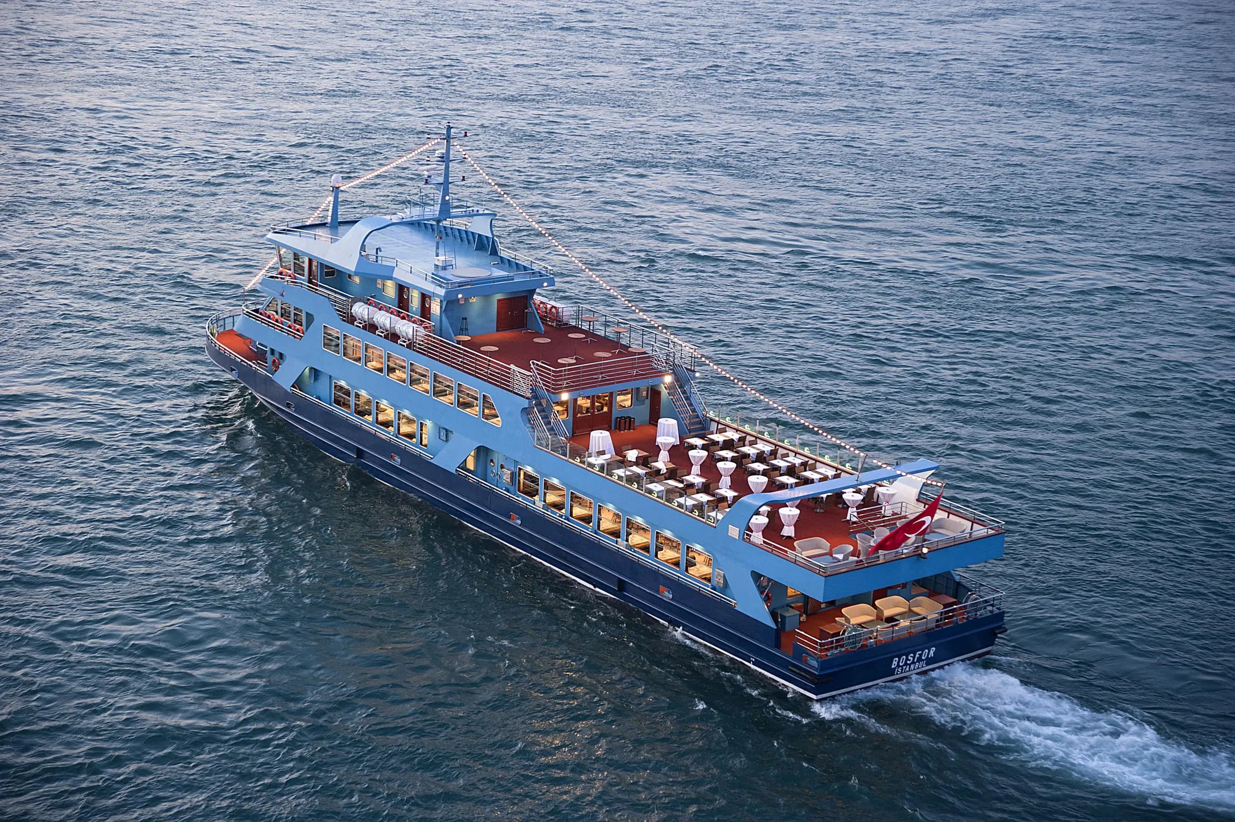 The BOSFOR from above in daylight, tables laid on the open aft deck and the ship's name on the hull